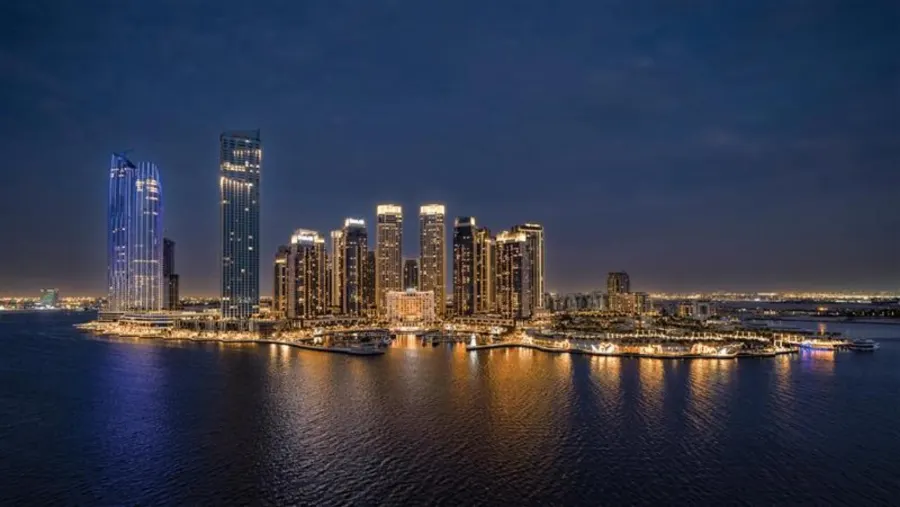 Photograph of Dubai Creek Harbour's towers lit at night, reflected in the creek